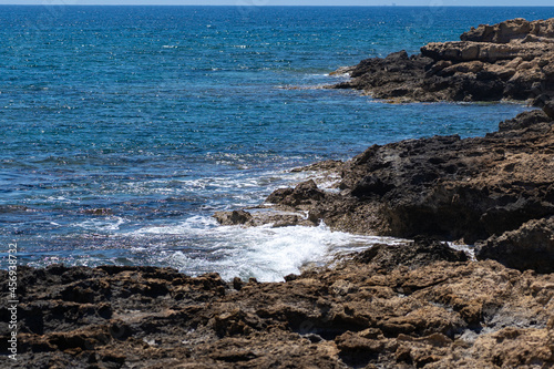 Sea surf, blue waves of Mediterranean sea in the Cyprus. Rocky stoned beach. Summer day. Sunny paradise. Sunny daytime seascape. View on the beach of Cyprus. Stones near mediterranean sea