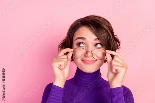 Photo of curious brunette young lady hold spectacles look empty space wear violet turtleneck isolated on pink background