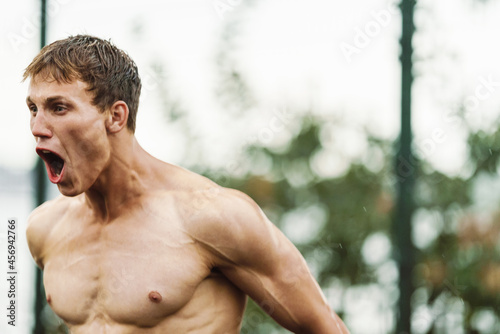 Young shirtless sportsman screaming while working out on playground