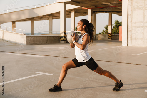 Black sportswoman doing exercise with medicine ball while working out