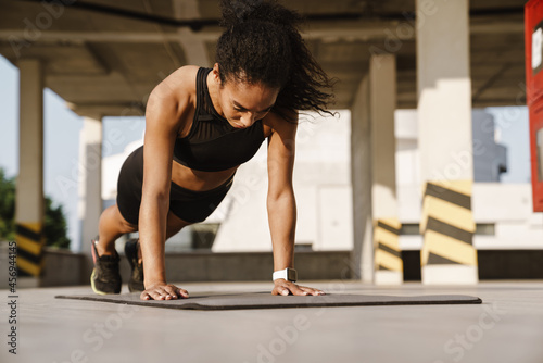 Black sportswoman working out on fitness mat on parking