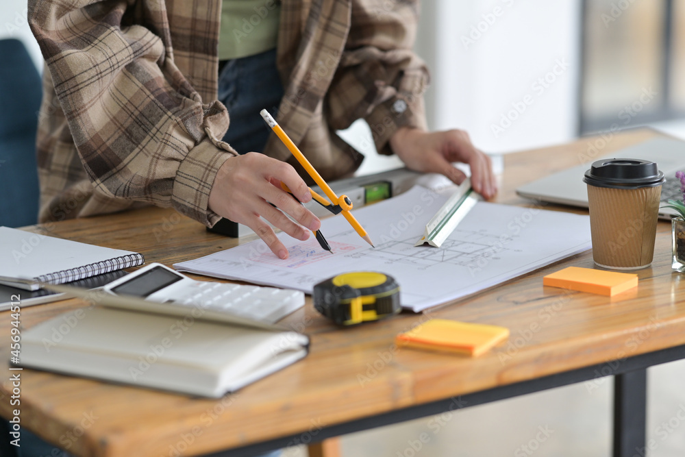 Cropped image of woman architect hands is drawing on a construction blueprint with a drawing compass and ruler. Cropped image of woman architect hands is drawing on a construction blueprint with a drawing compass and ruler.