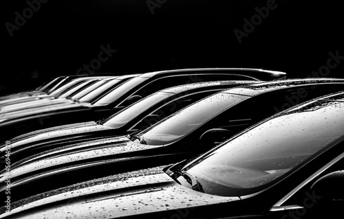 Black sedan cars standing in a row. Fleet of generic modern cars. Transportation. Luxury car fleet consisting of generic brandless design. isolated in dark background. after rain. wet surface. © Maxim Chuev