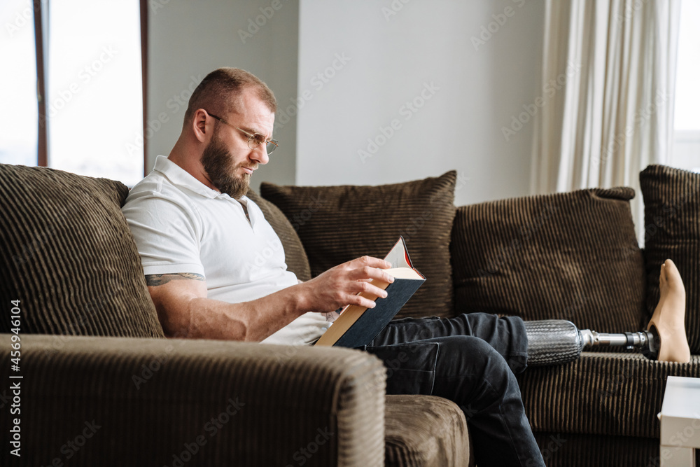 White man with prosthesis reading book while siting on couch at home