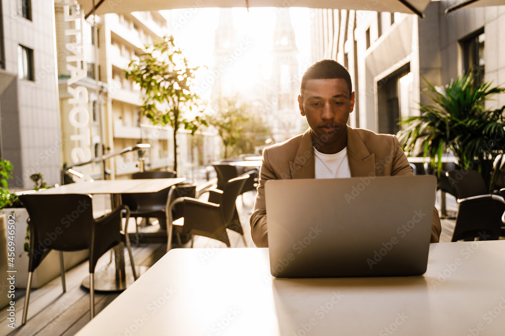 Black man working with laptop while sitting in cafe outdoors Black man working with laptop while sitting in cafe outdoors
