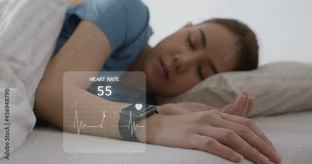 Asia teen woman wear smartwatch for sugar tracker, blood pressure tracking, resting sleep rate on arm IoT tech collect data app device relax body on cozy bed in future life at home.