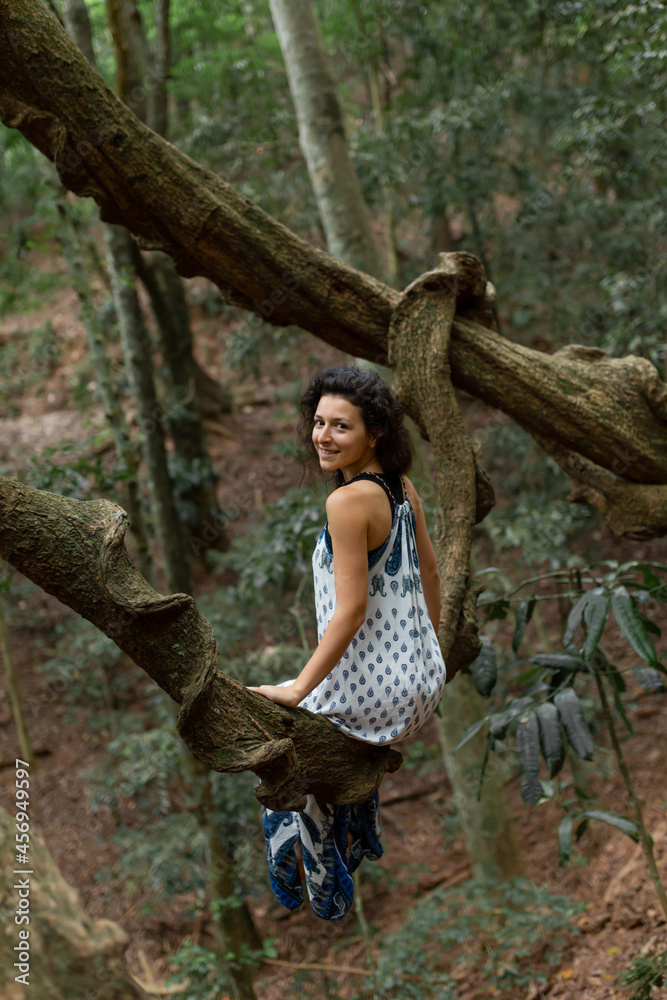 The girl sits on a huge liana tree branch in the jungle The girl sits on a huge liana tree branch in the jungle