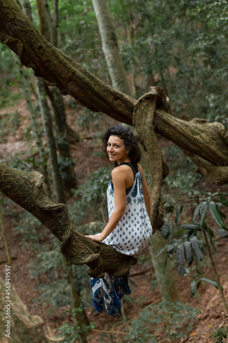 The girl sits on a huge liana tree branch in the jungle