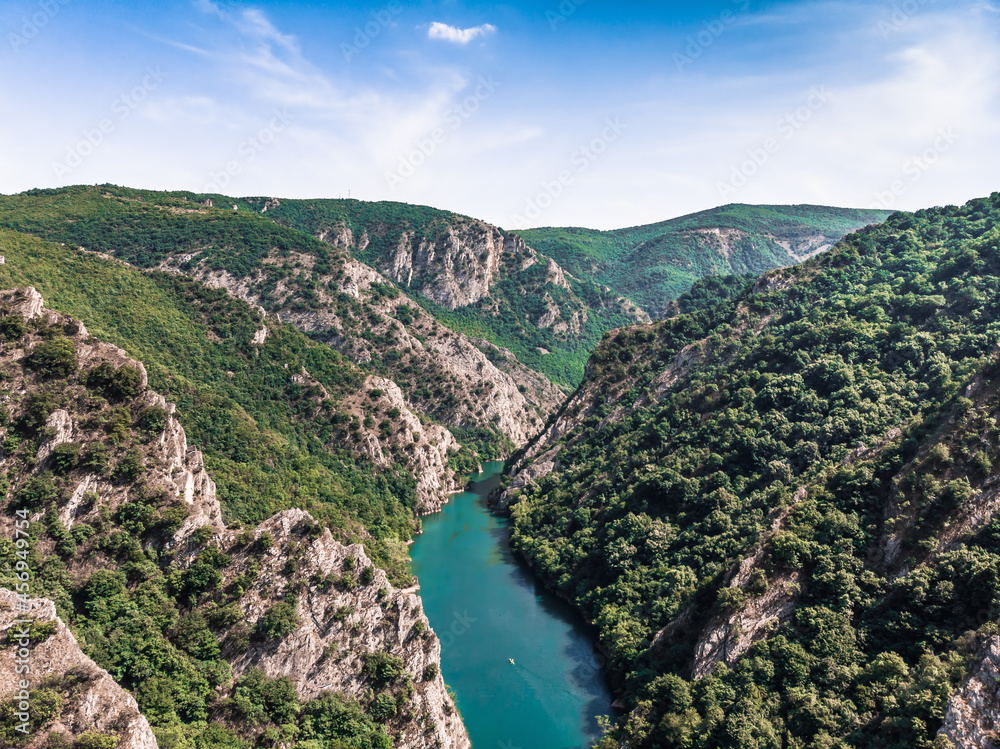 Drone view of Matka Canyon. Drone shot of a lake in a canyon in North Macedonia. Rocky green slopes. Transparent water surface of the lake. Mountain trail along the river. Lake in the mountains