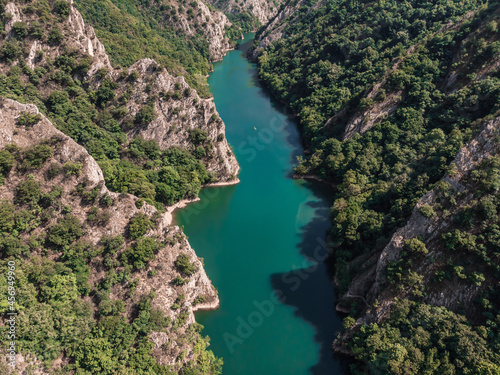 Drone view of Matka Canyon. Drone shot of a lake in a canyon in North Macedonia. Rocky green slopes. Transparent water surface of the lake. Mountain trail along the river. Lake in the mountains