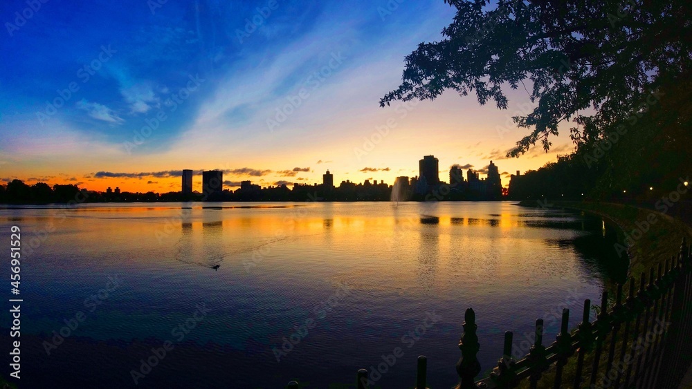 New York skyline at dawn as seen across the water of the Jackie Onassis Reservoir in Central Park, New York City.