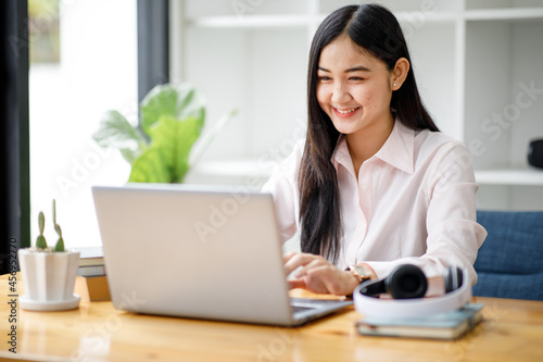 Young asian woman having conference video call using laptop talking to coworker online audience sitting at office desk in evening.	
