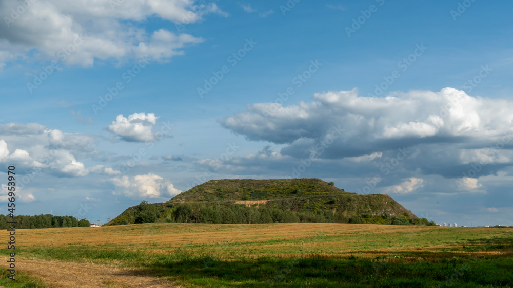 Obraz premium Closed city dump. Restoration of the territory. Landscaping of a large hill of garbage. In the background is a metropolis and a blue sky with clouds. Ecological problem.