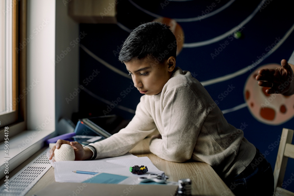 Autistic boy holding stress ball while reading book at home Autistic boy holding stress ball while reading book at home