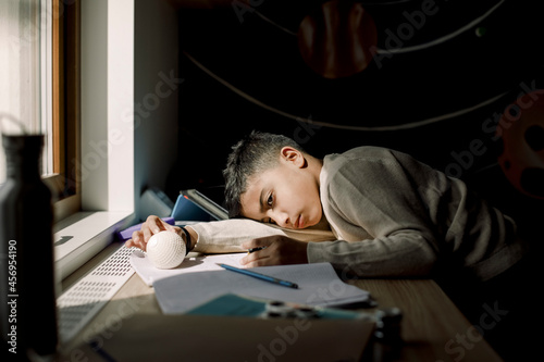 Tired pre-adolescent boy resting head on table in bedroom