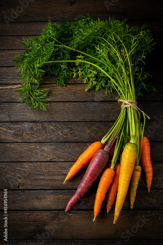 Colorful Rainbow carrot with their green leaves on wooden background, top view