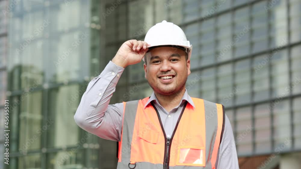 Smiling Asian engineer handsome man or architect looking camera with white safety helmet in construction site. Standing at modern building construction. Worker asian man working project building Smiling Asian engineer handsome man or architect looking camera with white safety helmet in construction site. Standing at modern building construction. Worker asian man working project building