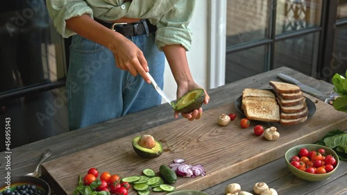 woman hands slicing green avocado on the wood board for preparing vegan full grain toast with mushrooms and vegetables outdoor on terrace healthy food concept 4K