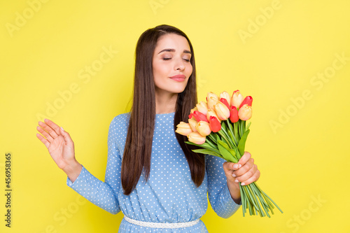 Photo of adorable sweet young woman dressed blue clothes enjoying bouquet aroma smiling isolated yellow color background