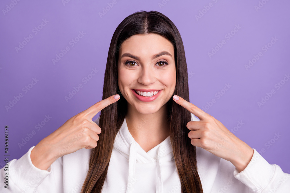 Photo of young positive happy woman point fingers face teeth whitening smile isolated on violet color background Photo of young positive happy woman point fingers face teeth whitening smile isolated on violet color background