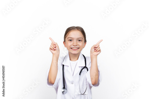 Smiling happy child girl in doctor's coat pointing at white background
