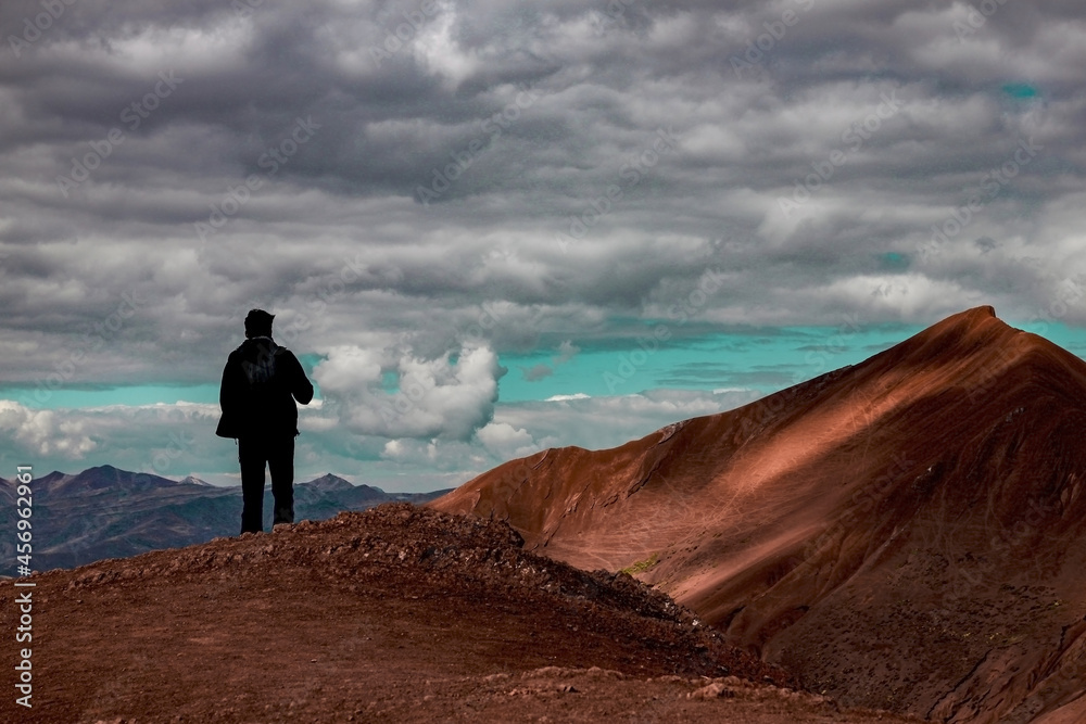 Silhouette of a man looking at a mountain. The sky has a lot of clouds and some clearing.