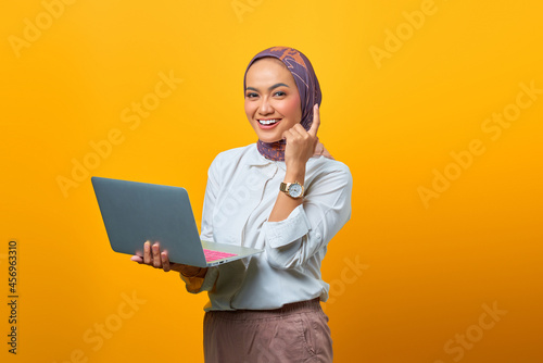 Portrait of smiling Asian woman holding laptop have good ideas over yellow background