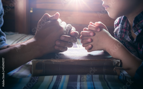 Close up hands of father and daughter praying on the Bible, focus hands.