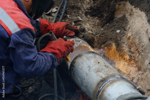 Plumber standing in pit is engaged in elimination of communal accident outdoors. Utility worker fixing broken water main. Welding work to replace rotten elements of water pipe. Sewerage pipe repair