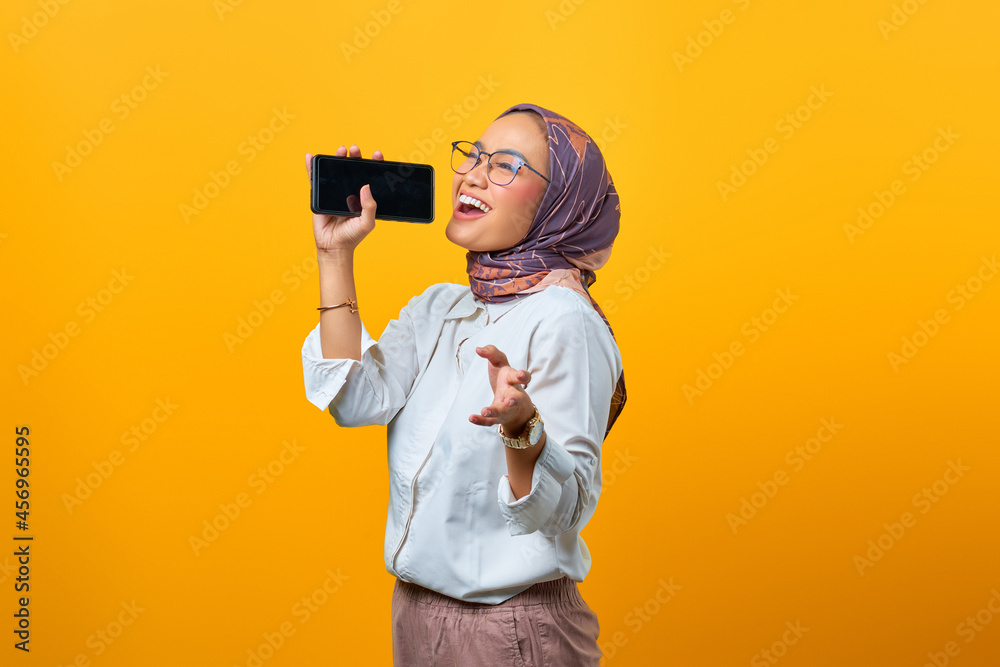 Beautiful Asian woman enjoying singing using smartphone over yellow background Beautiful Asian woman enjoying singing using smartphone over yellow background