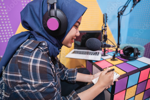 muslim woman is recording a podcast in studio with laptop taking a note with pen