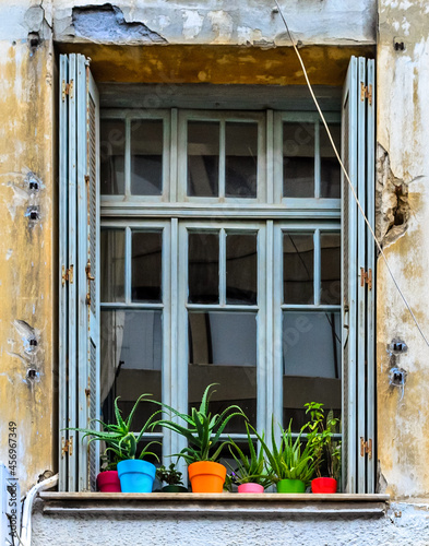 Vintage Window with Beautiful Colorful Potted Houseplants on thr Sill. Old House in Heraclion  Crete Island  Greece.