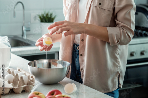 A woman in the kitchen breaks a chicken egg with a bowl. Cooking.