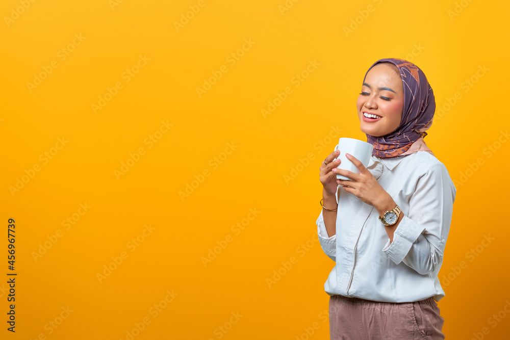 Portrait of beautiful Asian woman smiling and holding mug with blank space over yellow background Portrait of beautiful Asian woman smiling and holding mug with blank space over yellow background