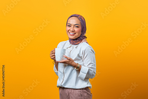 Portrait of beautiful Asian woman smiling and holding mug over yellow background