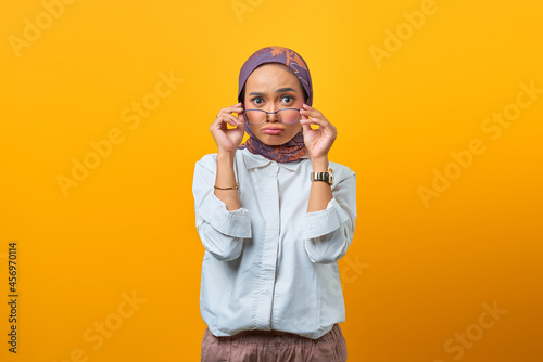 Attractive Asian woman holding eyeglasses with both hand over yellow background
