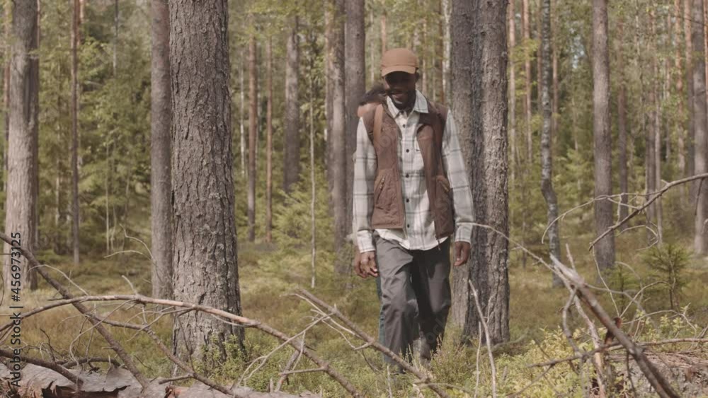 Tracking slowmo shot of happy young African-American couple in casualwear walking through summer forest Tracking slowmo shot of happy young African-American couple in casualwear walking through summer forest