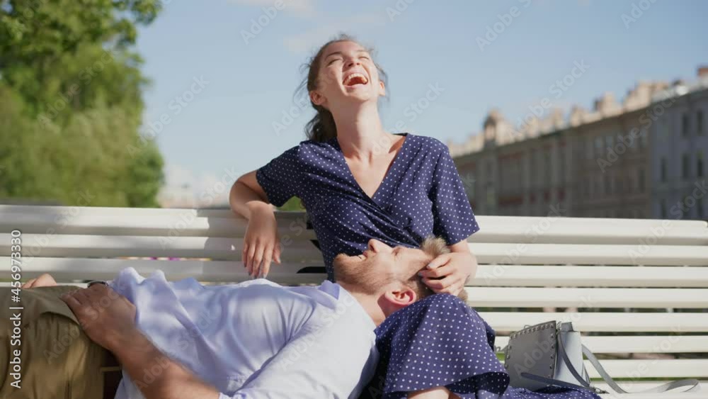 Young man lying on girlfriend lap relaxing together on bench outdoors