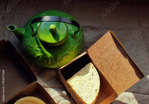 Homemade farm piece of cheese in box and green teapot on the table 