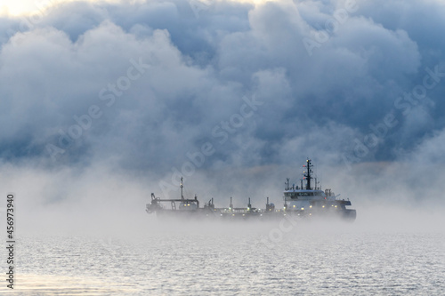 Vessel engaged in dredging. Dredger working at sea. Ship excavating material from a water environment. Strong fog in Arctic sea. Construction Marine offshore works. Dam building, crane, barge, dredger © Alexey Seafarer