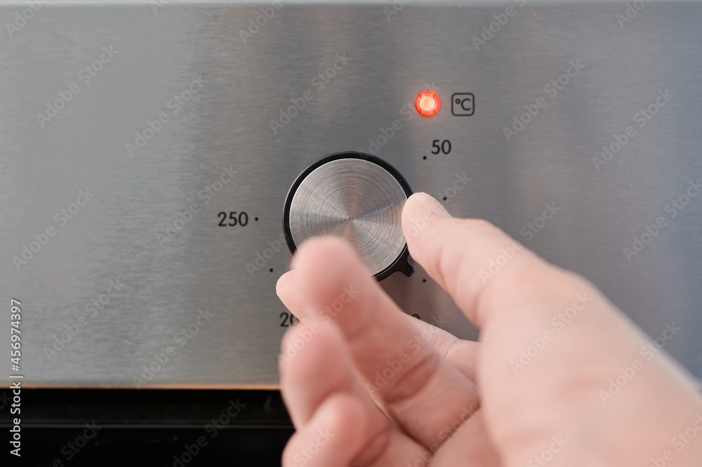 Fototapeta premium Picture about energy consumption, a man's hand turning an oven thermostat