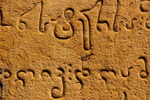 Close-up Ancient carving of Mkhedruli alphabet developed between the 11th and 13th centuries - official language of Georgia - on old grainy sandstone wall. photo