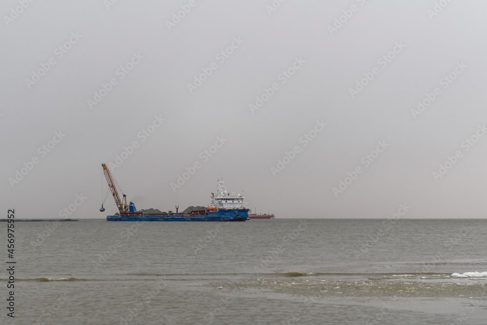 Vessel engaged in dredging. Dredger working at sea. Ship excavating material from a water environment. Strong fog in Arctic sea. Construction Marine offshore works. Dam building, crane, barge, dredger