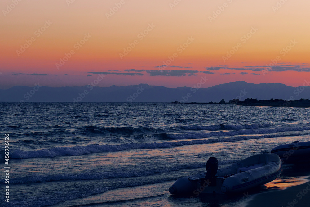 Sunset on the sea coast with mountains in the background and inflatable boat in the foreground.