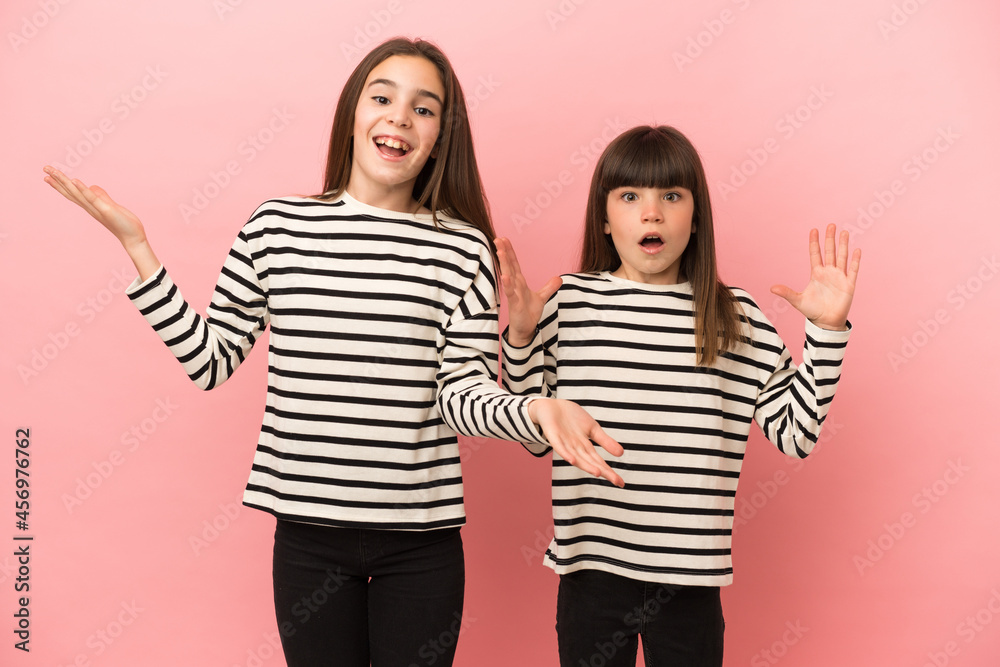 Little sisters girls isolated on pink background with surprise and shocked facial expression Little sisters girls isolated on pink background with surprise and shocked facial expression