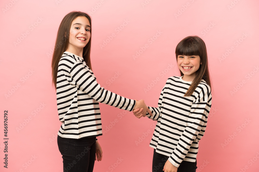 Little sisters girls isolated on pink background handshaking after good deal Little sisters girls isolated on pink background handshaking after good deal