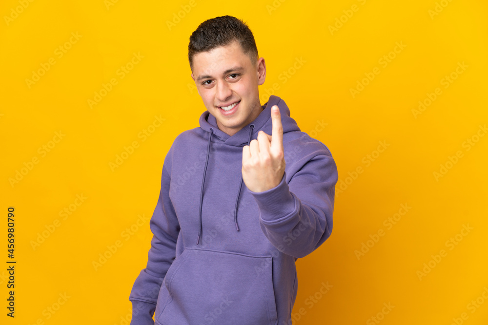 Young caucasian man isolated on yellow background doing coming gesture Young caucasian man isolated on yellow background doing coming gesture