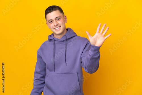 Young caucasian man isolated on yellow background counting five with fingers