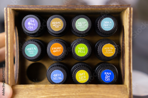 aroma oil concept. Top view essential oils in a bottle with black cap multicolored stickers named on Russian. Wooden storage box with compartment. soft grey background. Aromatic set of 12 pieces.