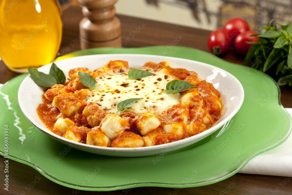 nhoque ao molho de tomate com queijo mussarela derretido e folhas de manjericão, em mesa decorada.